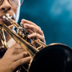 cropped shot of male musician playing on trumpet on stage with dramatic lighting and smoke